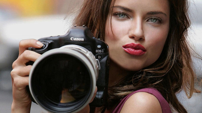 Adriana Lima lanzando un beso con una cámara profesional en sus manos 