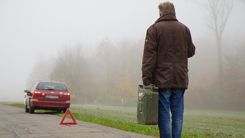 Hombre frente a un coche averiado y un triángulo de señalización con una botella de gasolina